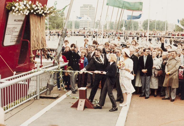Kroonprins Willem Alexander onthult op aanwijzing van burgemeester André van der Louw in aanwezigheid van Koningin Beatrix de gedenkplaquette. Prins Willem Alexander trekt aan het touw om de plaquette te onthullen, Koningin Beatrix kijkt toe met een menigte op de achtergrond