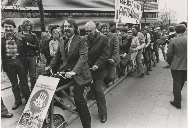 25 april 1978: Het College van Burgemeester en Wethouders maken reclame voor de Rotterdamse fietsvierdaagse op 1,2,3, en 4 mei 1978. Het gezelschap poseert op een elfpersoonsfiets voor het Gemeentelijk Rekencentrum aan de Stationssingel. Op de foto o.a. burgemeester André van der Louw, de wethouders J.G. van der Ploeg, Mentink, Schmitz, Van der Have, Riezenkamp, Mastik en Van der Pols. Foto: Rotterdams Nieuwsblad. Collectie 4282, 1978-1370-kl