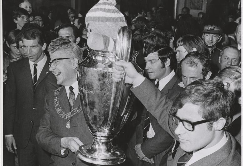 7 mei 1970: Rinus Israël aanvoerder van Feyenoord en burgemeester Thomassen presenteren trots de Europacup I. Feyenoord is de eerste Nederlandse club die de Europacup I wist te winnen. In de finale versloegen zij, na verlenging, het Schotse Celtic met 2-1. In de cup zit de Celtic-mascotte, een gebreide pop van een halve meter hoog in de clubkleuren groen-wit, die de aanvoerder van de Schotse club cadeau had gedaan aan Feyenoord. Fotograaf Hans Vrijmoet. Collectie 4282, 1970-725-kl