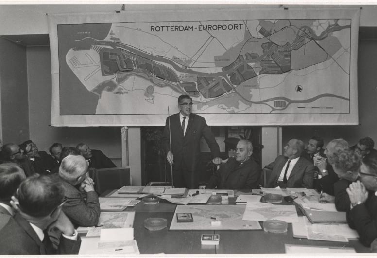 28 juni 1966: In een vergadering van de wijkraad voor Hoek van Holland geeft burgemeester Thomassen uitleg over de uitbreidingsplannen van de Rotterdamse haven tussen Hoek van Holland en Maassluis. Vanuit het Westland werden grote bezwaren geuit tegen dit voornemen. Uiteindelijk komt het plan voor deze Rijnpoorthaven nooit tot uitvoering; dit besluit valt echter pas eind 1975. Fotograaf Robert Lantos, collectie 4282-XXXIII-1577-01-kl
